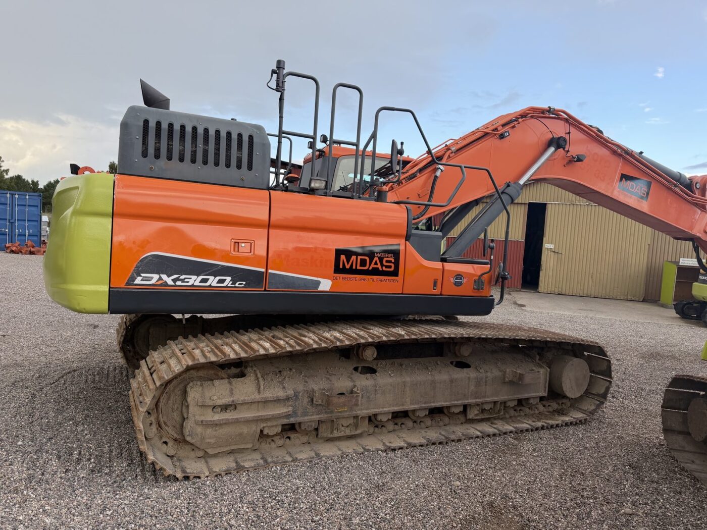 Doosan DX 300 LC set fra højre side med DX300LC-mærkning og MDAS Materiel-logo, kontravægt til venstre og hævet bom til højre
