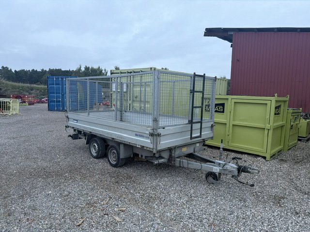 Varianttip trailer med gittersider set skråt forfra fra trækstangens side, parkeret på en grusplads foran containere